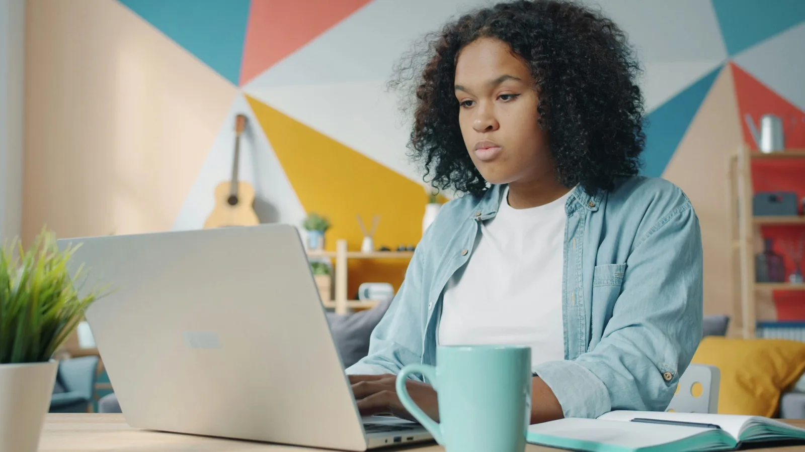 A learner using a laptop beside an open notebook